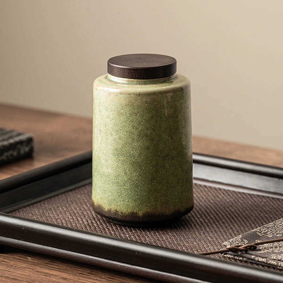 Tall green ceramic tea caddy on a dark wooden tray