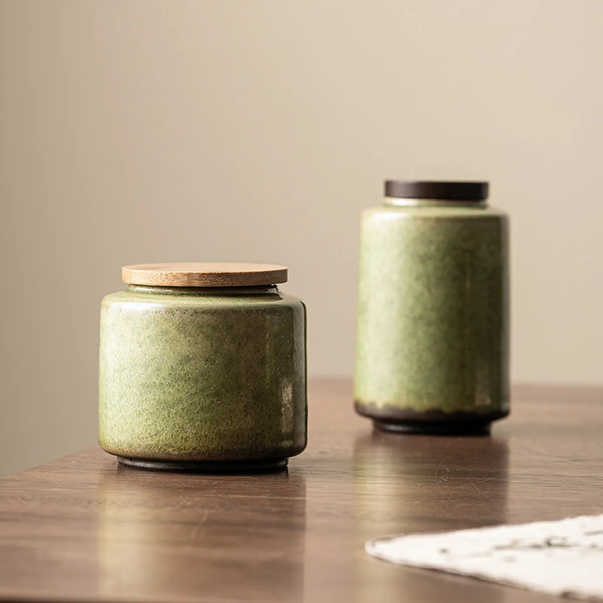 The short and tall green tea caddies side by side on a wooden table