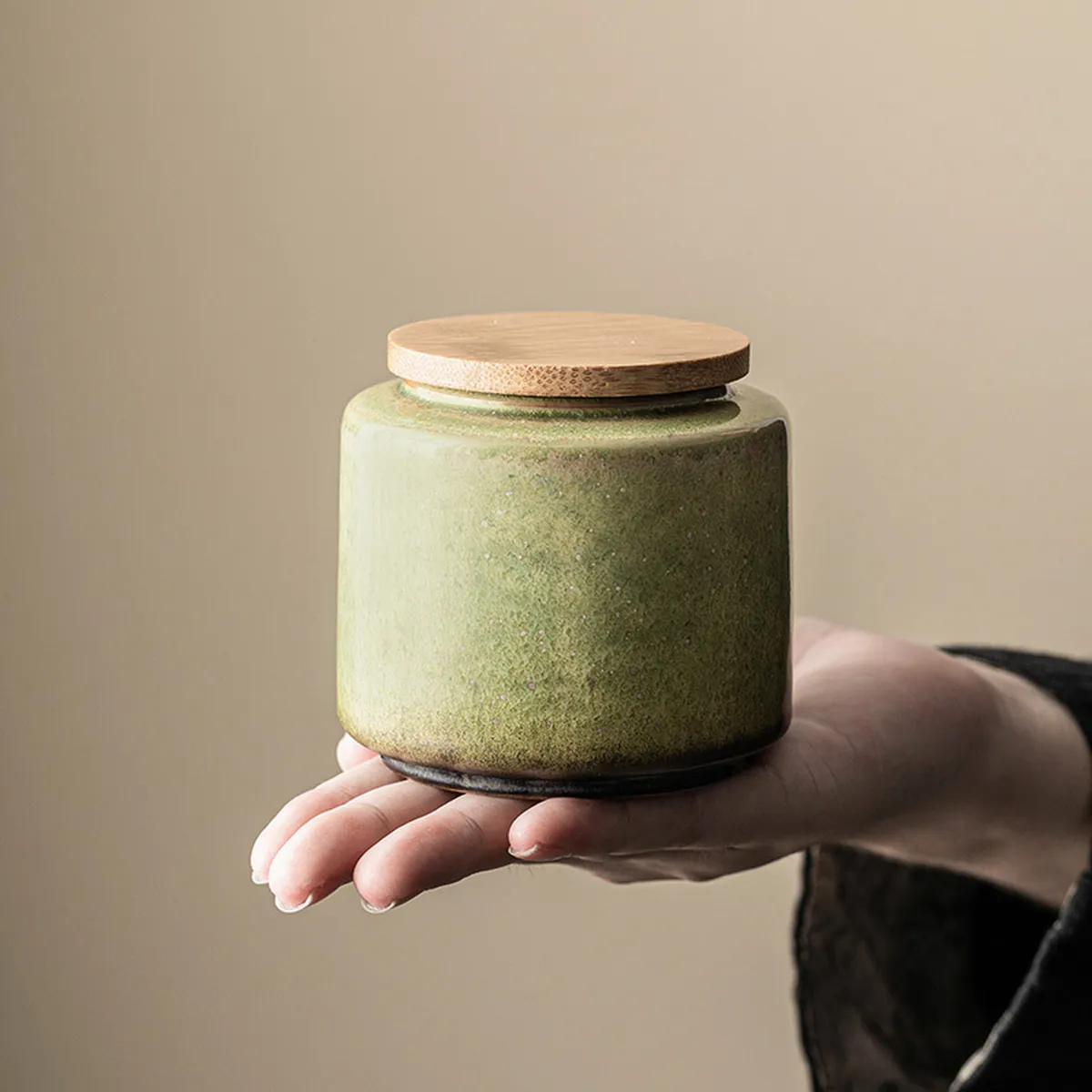 Green tea caddy with wooden lid held in the palm of a hand