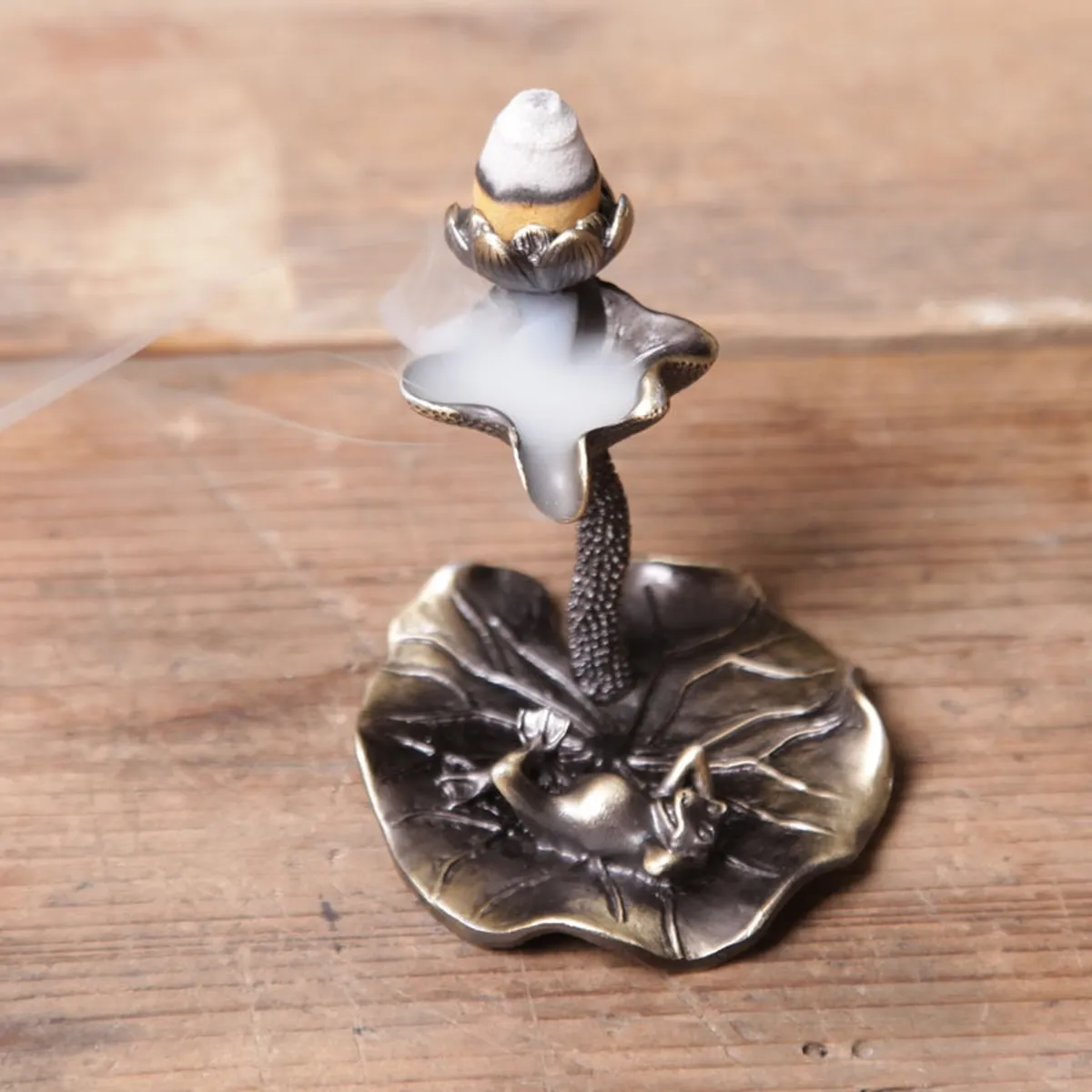 The lotus burner with a lit cone, smoke flowing down onto the leaf