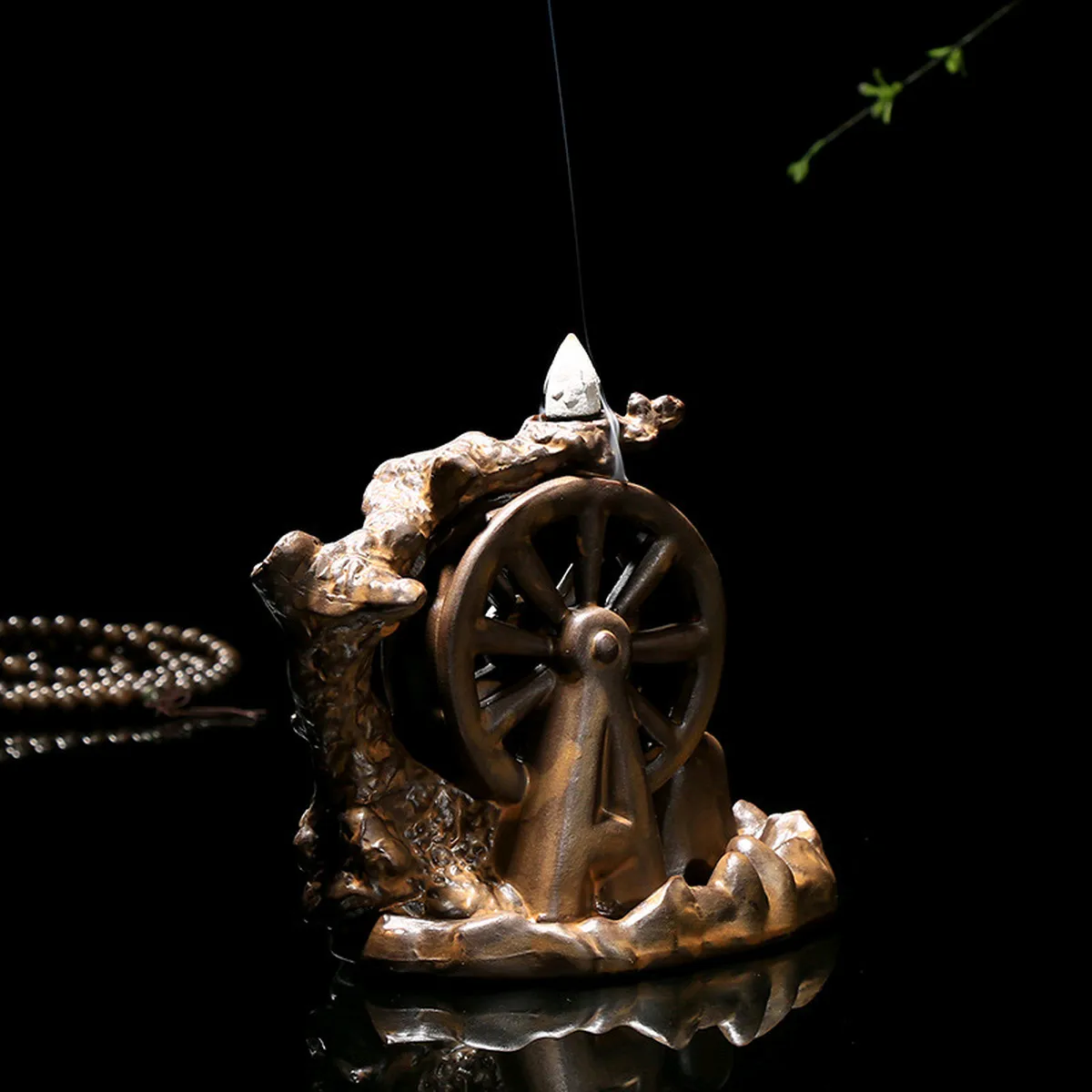 Ceramic water-wheel incense burner with a lit cone, dark background
