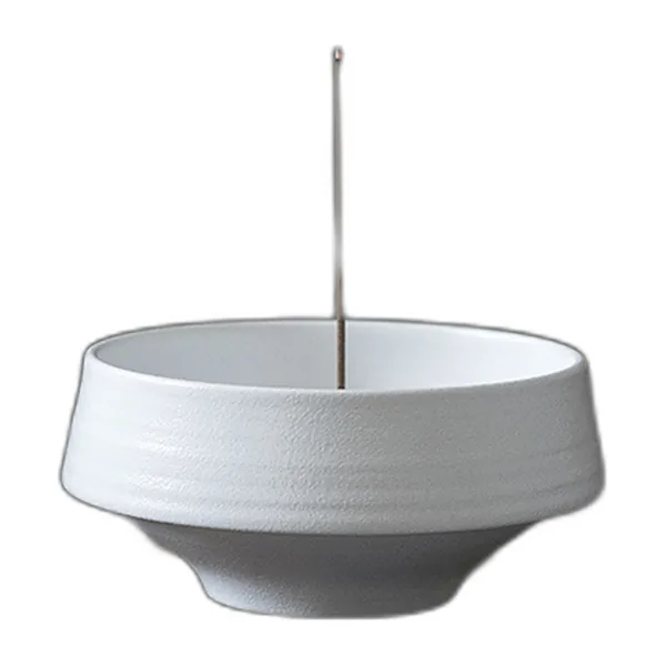 White ceramic incense bowl on a narrow foot with an incense stick standing in the centre