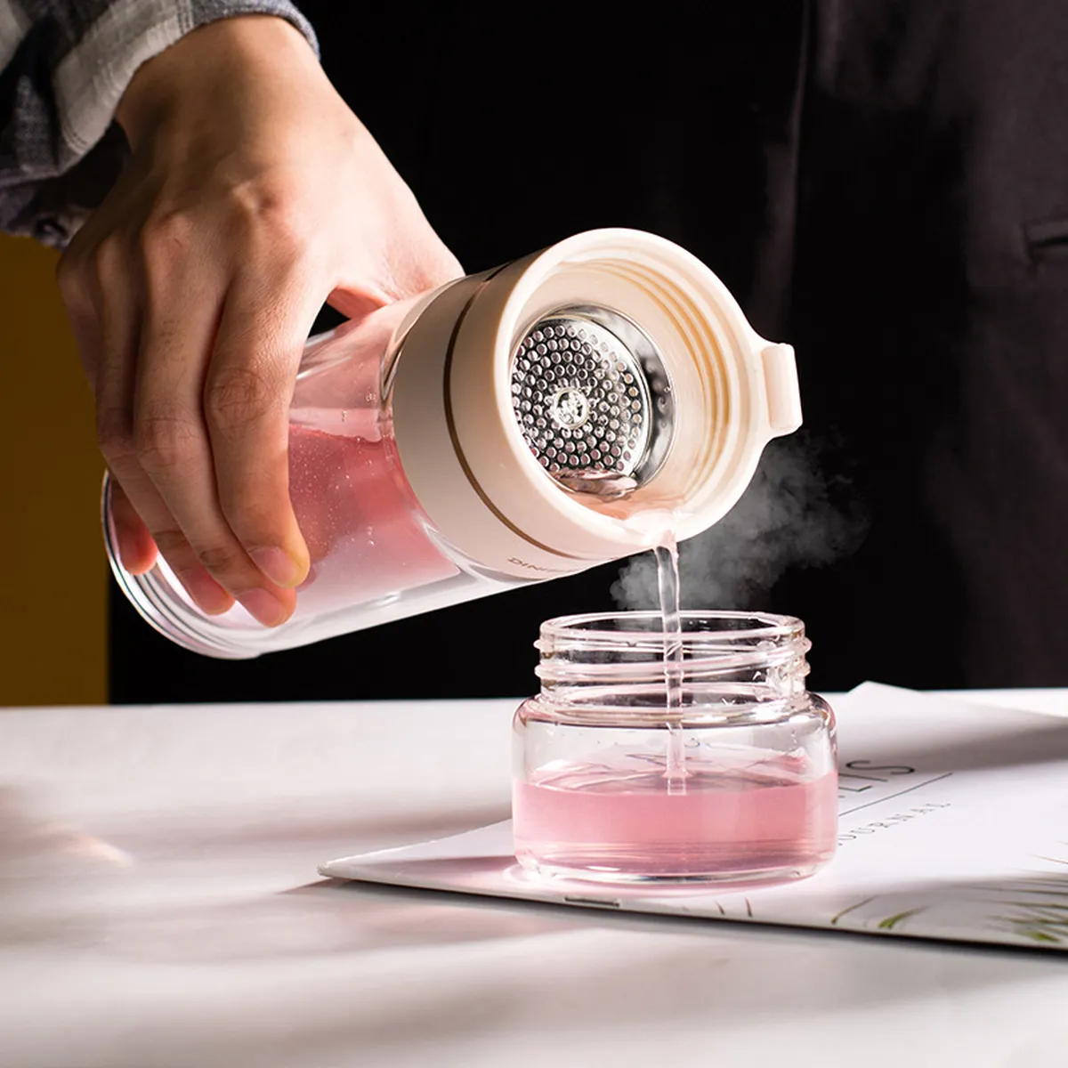 Pink tea bottle pouring hot tea, steel filter visible