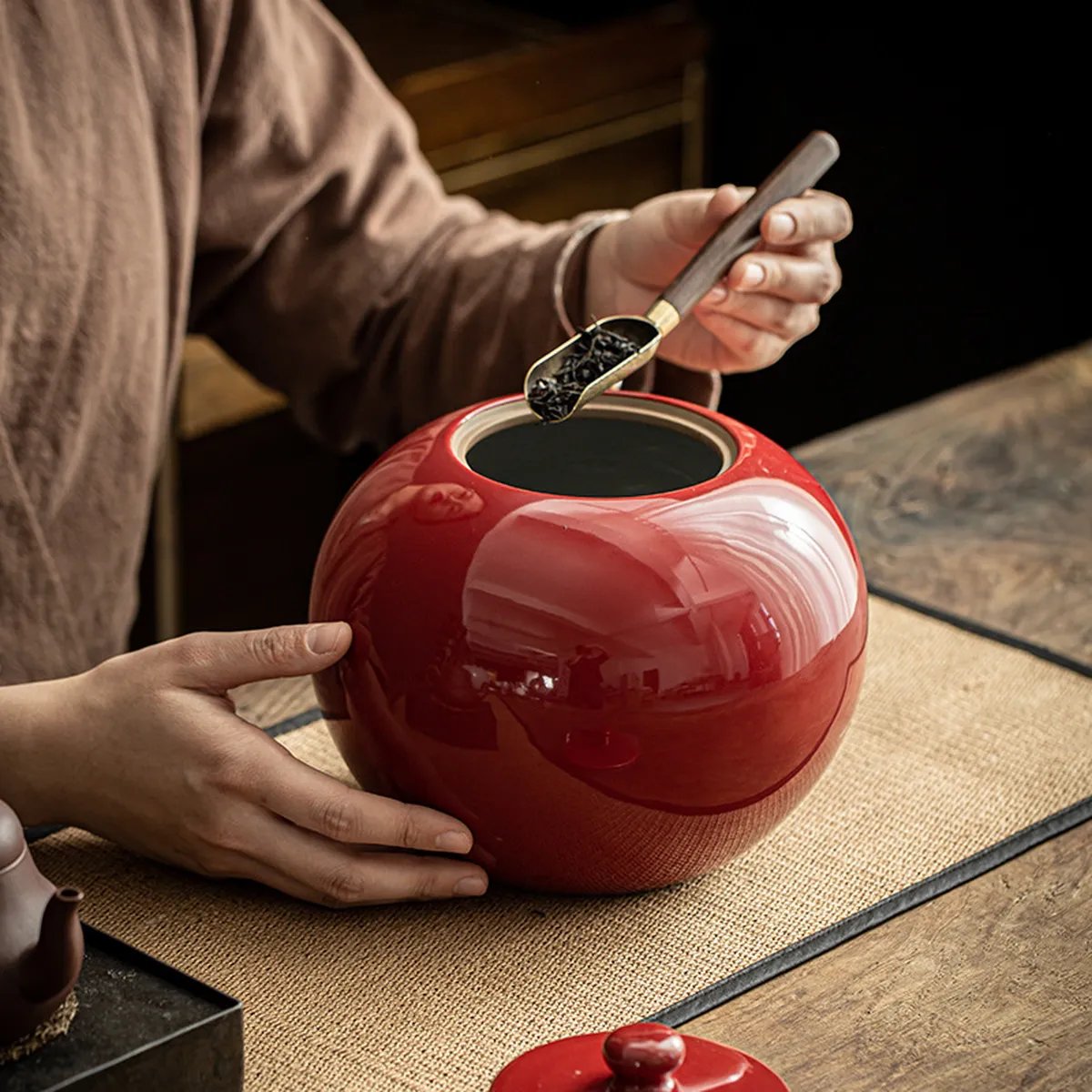 Large red tea jar open, tea leaves being scooped with a spoon