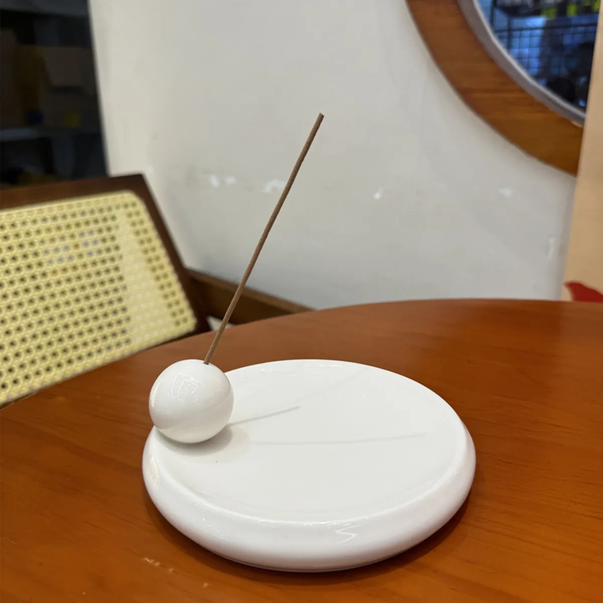 White ceramic ball incense holder with a stick, on a round table