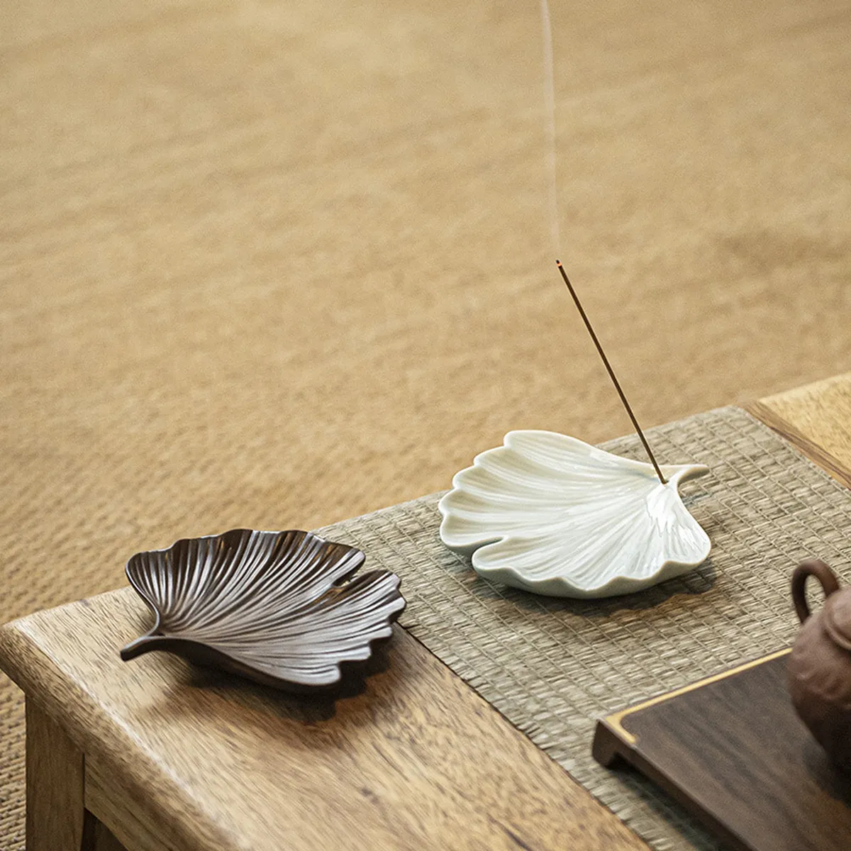 Two ginkgo leaf incense holders, brown and celadon, on a rush mat