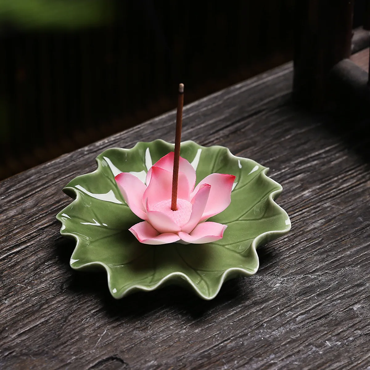 Pink lotus incense holder on its green leaf with a stick, on a dark table
