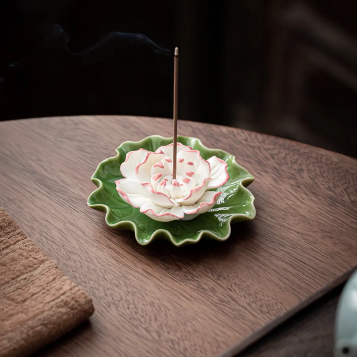 White lotus incense holder on a green leaf, smoke rising