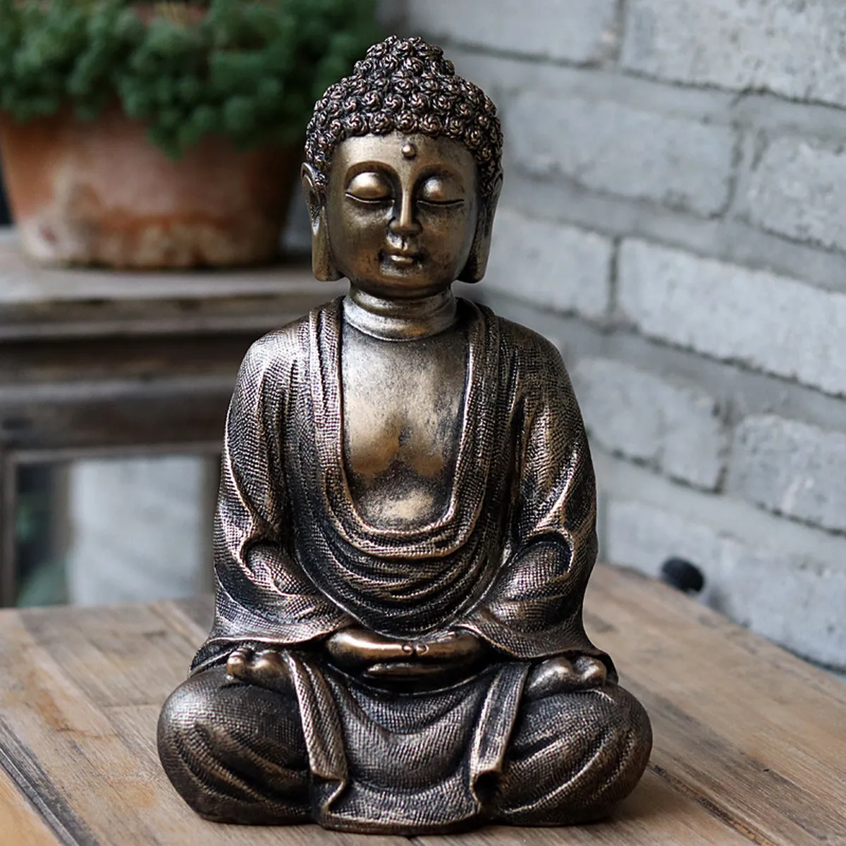 Meditating Buddha figurine on a wooden table in front of a brick wall