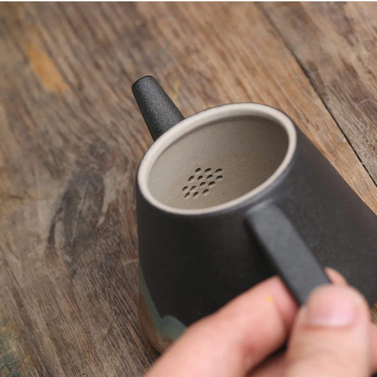 The teapot in hand, showing the pierced filter at the spout