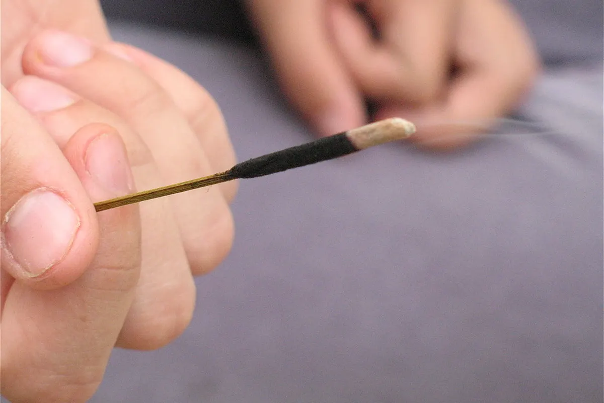 A lit incense stick held between the fingers